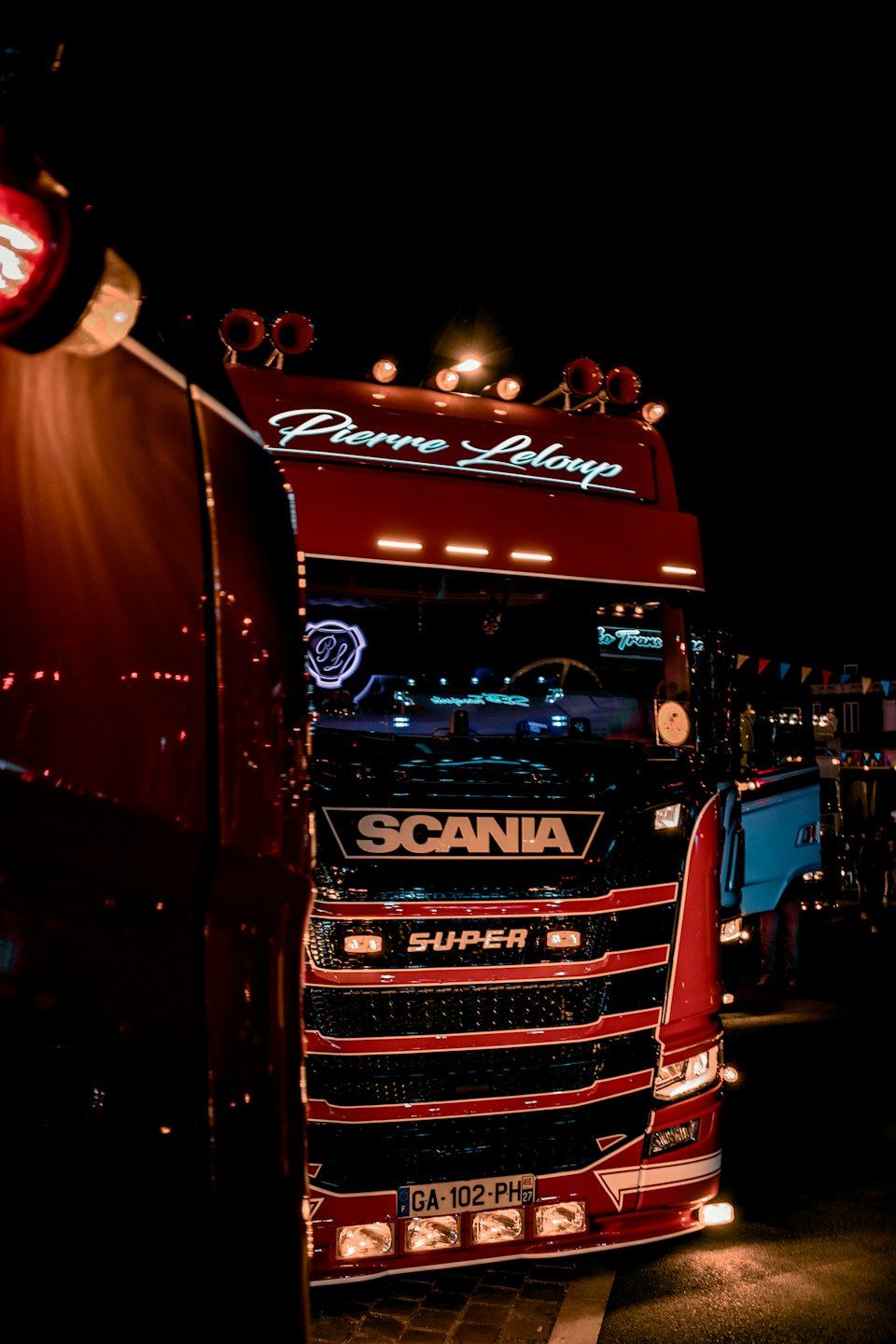 Röd och svart Scania-lastbil på natten med starka ljus.